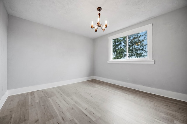 empty room featuring a textured ceiling, wood finished floors, baseboards, and a chandelier