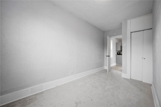 unfurnished bedroom with light colored carpet, a closet, a textured wall, and a textured ceiling