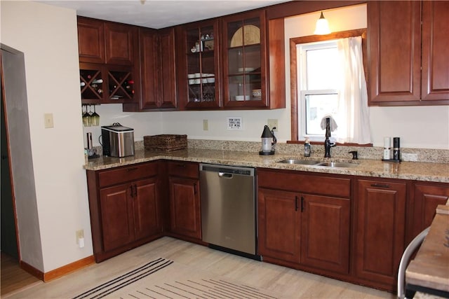 kitchen with a sink, baseboards, glass insert cabinets, light stone countertops, and dishwasher