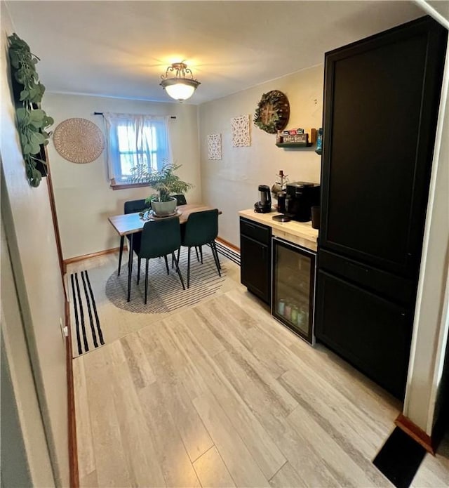 dining room with light wood-type flooring, wine cooler, a bar, and baseboards