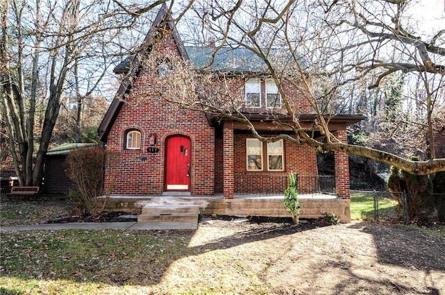 tudor-style house featuring a gate, brick siding, and fence