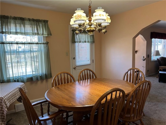 carpeted dining room featuring arched walkways and an inviting chandelier