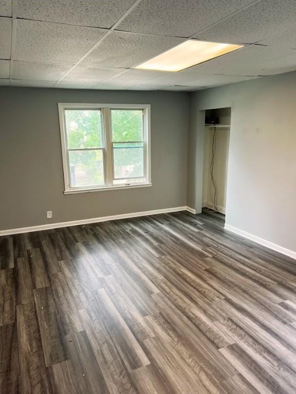 unfurnished room with a paneled ceiling, dark wood-type flooring, and baseboards