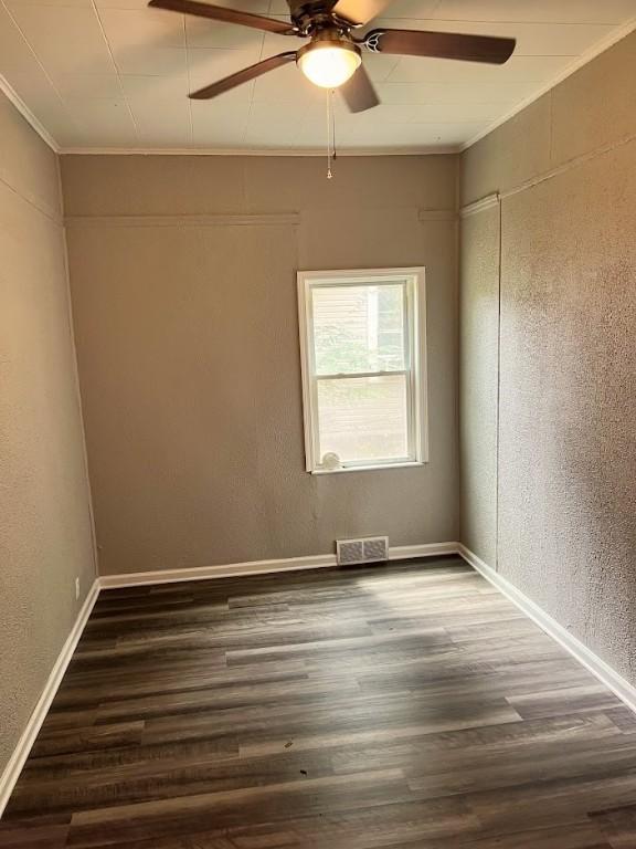 empty room featuring a ceiling fan, wood finished floors, visible vents, baseboards, and crown molding