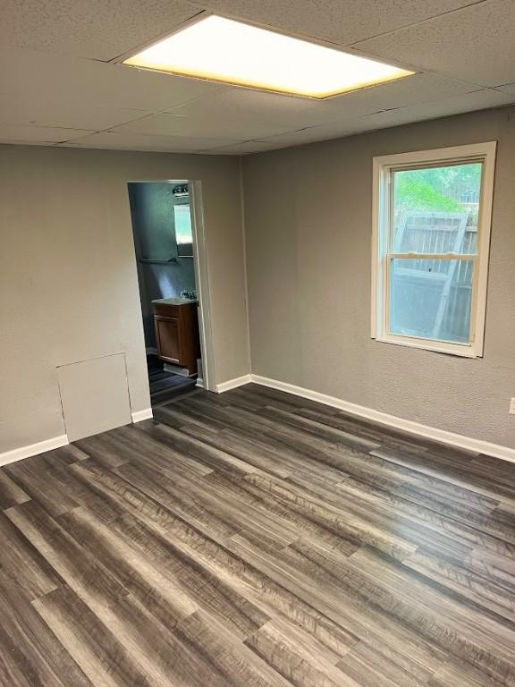 unfurnished room featuring a drop ceiling, baseboards, and dark wood-style flooring