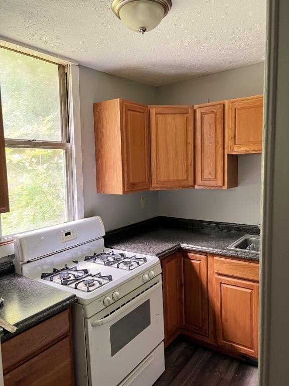 kitchen featuring dark countertops, white gas stove, brown cabinets, a textured ceiling, and dark wood-style flooring