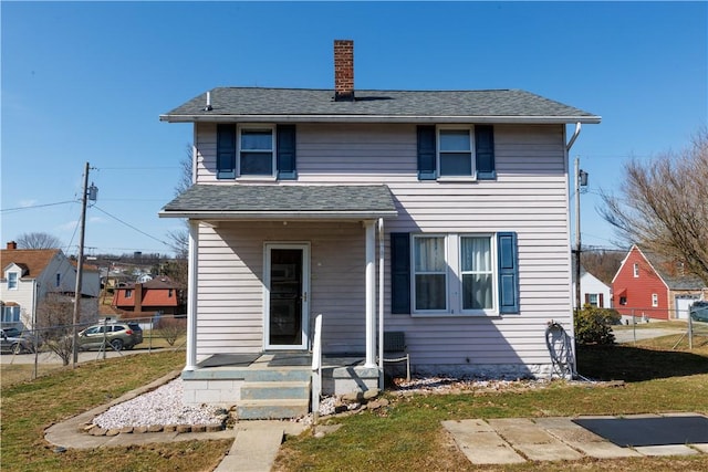 traditional-style house featuring a front yard, roof with shingles, a chimney, and fence