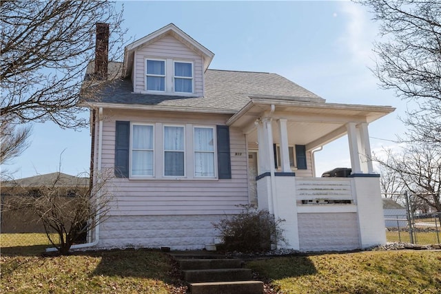 bungalow-style home with a porch, a front lawn, roof with shingles, and a chimney