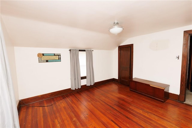 spare room featuring dark wood-type flooring, baseboards, and lofted ceiling