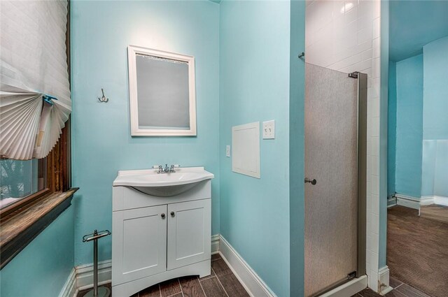 bathroom with wood finish floors, baseboards, walk in shower, and vanity