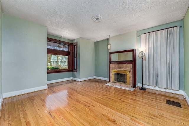 unfurnished living room with visible vents, a brick fireplace, baseboards, and wood-type flooring