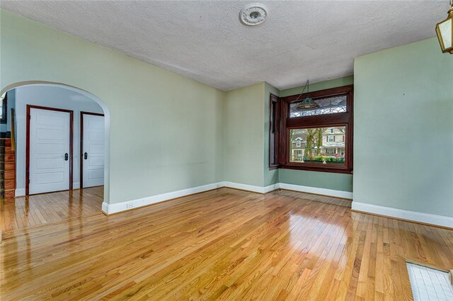 empty room with hardwood / wood-style flooring, baseboards, arched walkways, and a textured ceiling