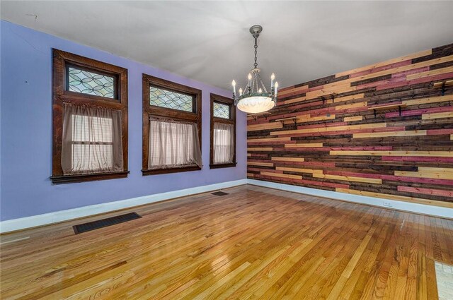 unfurnished room featuring visible vents, an accent wall, baseboards, and wood finished floors