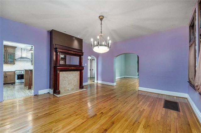 unfurnished living room with arched walkways, visible vents, light wood-type flooring, and baseboards