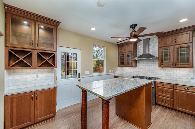 kitchen with high end range, light stone countertops, light wood finished floors, a kitchen island, and wall chimney range hood