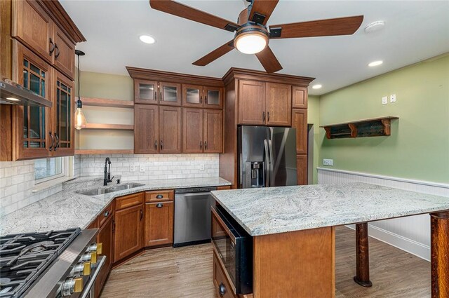 kitchen featuring light wood finished floors, a sink, a wainscoted wall, stainless steel appliances, and open shelves