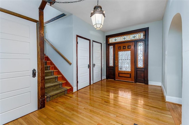 foyer with arched walkways, stairs, light wood-type flooring, and baseboards