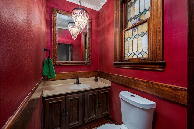 half bath with a notable chandelier, toilet, vanity, and crown molding