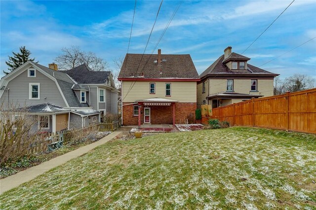 back of house featuring a lawn, a chimney, brick siding, and fence