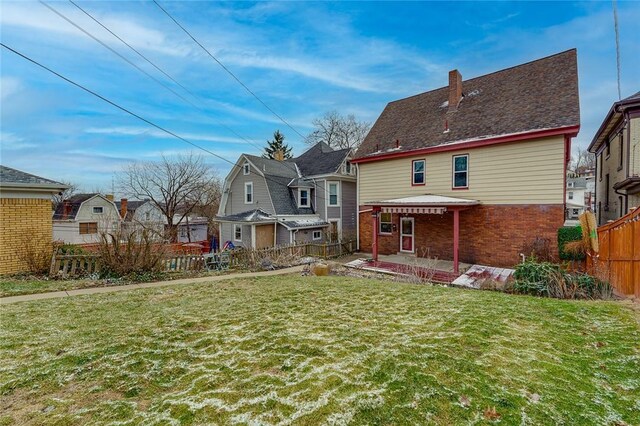 rear view of house featuring brick siding, a lawn, a chimney, and fence