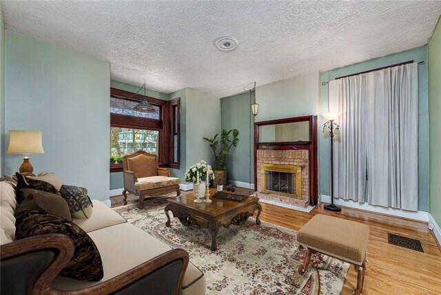 living area featuring visible vents, a textured ceiling, wood finished floors, baseboards, and a brick fireplace