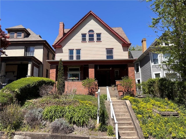 view of front of house featuring stairs, a chimney, a porch, and brick siding