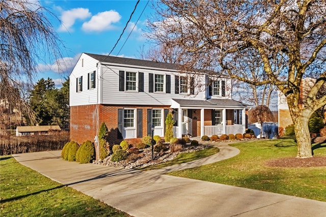 colonial house with brick siding, a porch, concrete driveway, and a front lawn