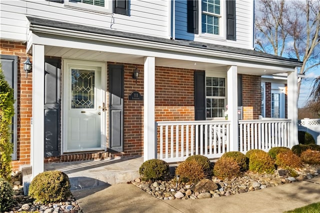 doorway to property featuring brick siding and a porch