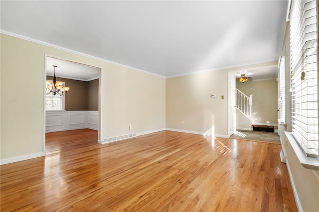 unfurnished living room with light wood-type flooring, visible vents, stairway, crown molding, and a chandelier