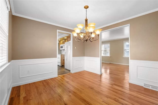 unfurnished dining area with a wainscoted wall, crown molding, light wood-style floors, and visible vents