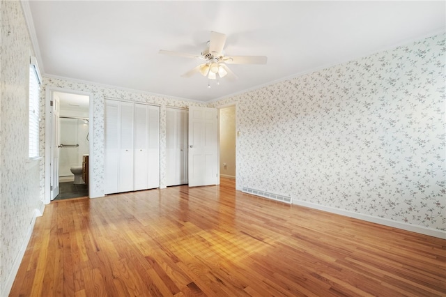 unfurnished bedroom featuring visible vents, wood finished floors, and wallpapered walls