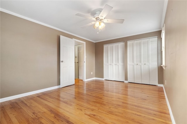 unfurnished bedroom with crown molding, baseboards, light wood-type flooring, and multiple closets