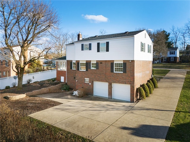 exterior space featuring brick siding, fence, a chimney, a garage, and driveway