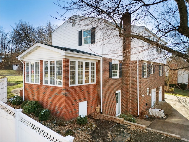 view of property exterior featuring a sunroom, brick siding, a chimney, and fence