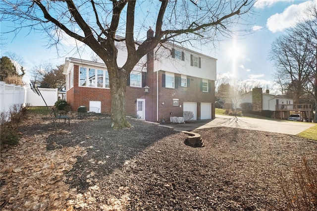 back of property with fence, a chimney, concrete driveway, a garage, and brick siding