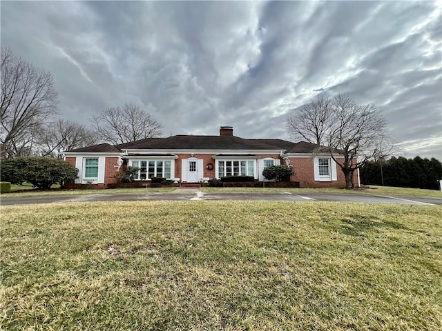 view of front of property featuring aphalt driveway, brick siding, and a front lawn