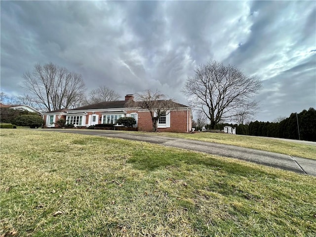 ranch-style home featuring brick siding, a chimney, aphalt driveway, and a front lawn