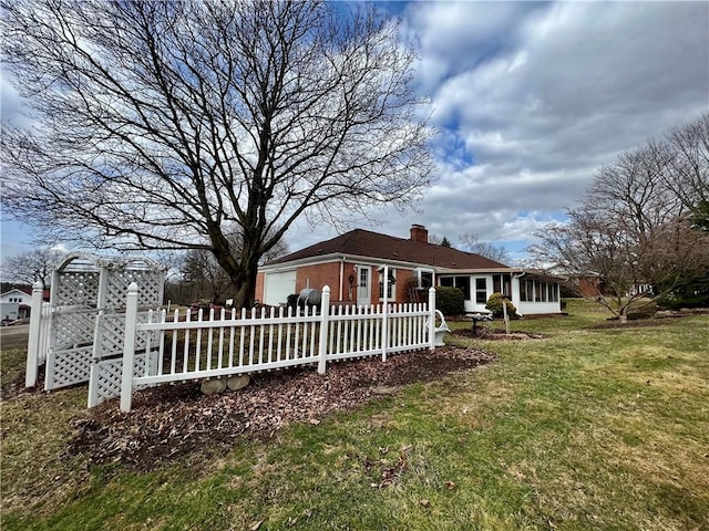 exterior space featuring a fenced front yard, a yard, a sunroom, brick siding, and a chimney