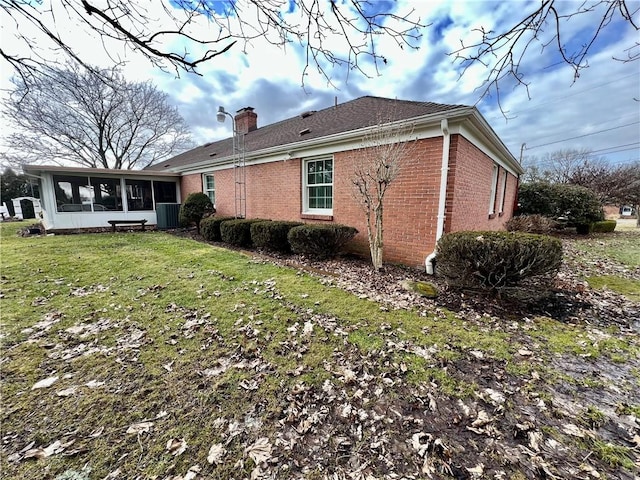 view of side of home with brick siding, a chimney, a yard, and a sunroom