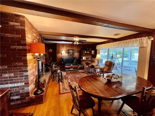 dining room with light wood finished floors, visible vents, a brick fireplace, beamed ceiling, and a ceiling fan