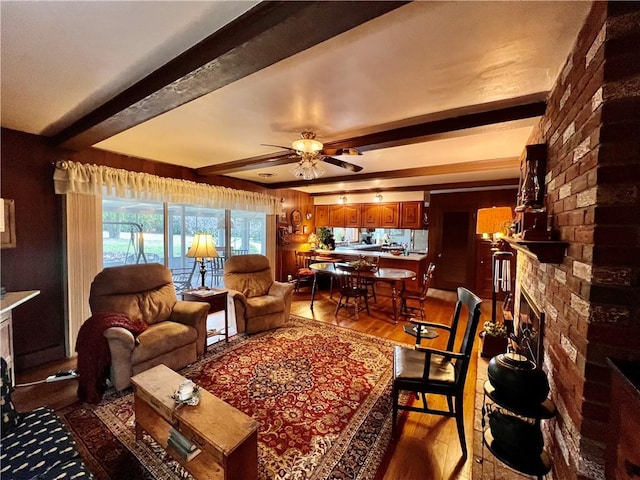 living area with beamed ceiling, dark wood-type flooring, brick wall, a fireplace, and ceiling fan