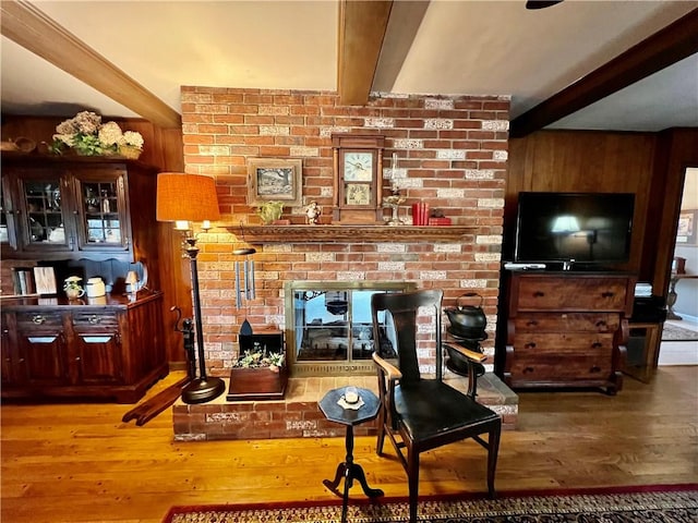 living room featuring beamed ceiling, wood finished floors, a fireplace, and wood walls