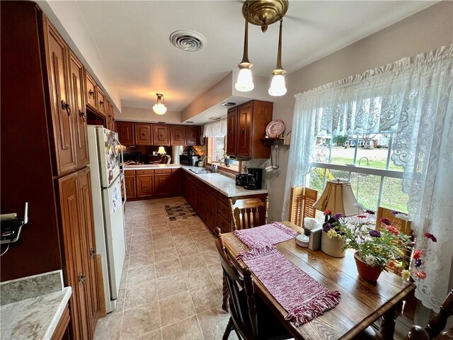 kitchen featuring visible vents, freestanding refrigerator, a sink, light countertops, and a wealth of natural light