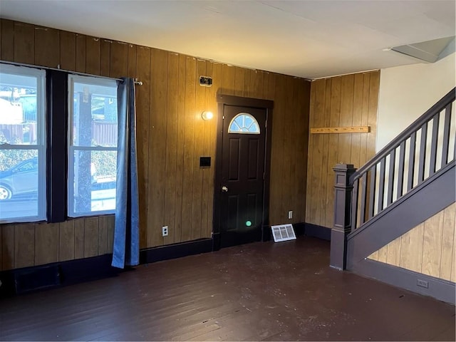 foyer featuring visible vents, stairs, wooden walls, and wood finished floors