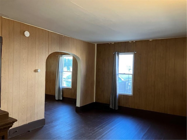 spare room with arched walkways, wood walls, and dark wood-style flooring