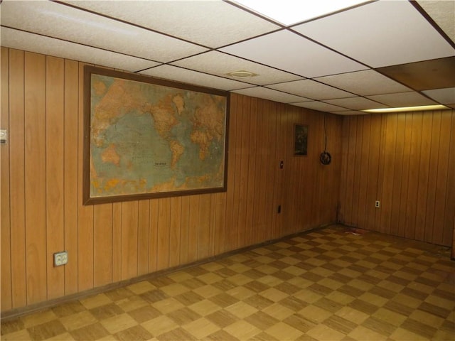 empty room featuring a drop ceiling, baseboards, light floors, and wooden walls