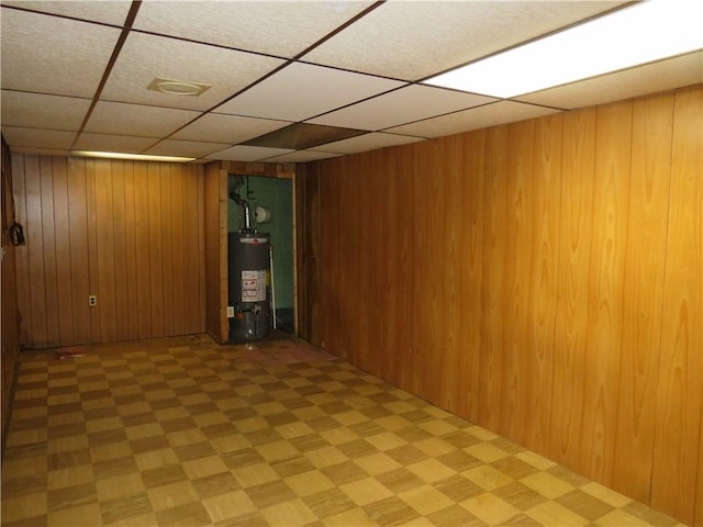 finished basement with gas water heater, a drop ceiling, and wooden walls