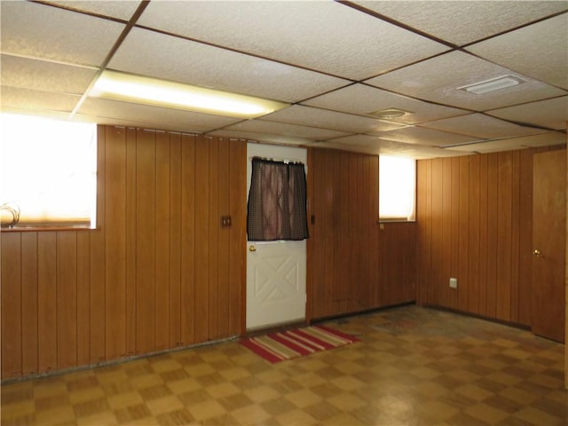 basement featuring visible vents, light floors, a paneled ceiling, and wood walls