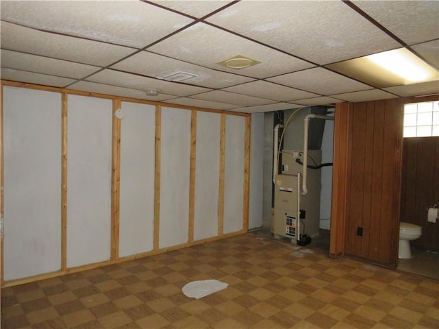 below grade area with heating unit, a drop ceiling, and light floors