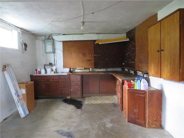 kitchen with concrete block wall, unfinished concrete floors, electric panel, and brown cabinets